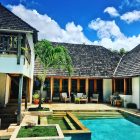 Elegant villa with wooden accents and a pristine pool under a bright blue sky.