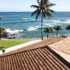 Ocean view with palm trees and a rooftop in the foreground.