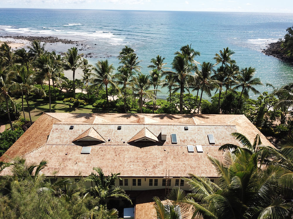 Aerial view of oceanfront house with palm trees and beach in the background.